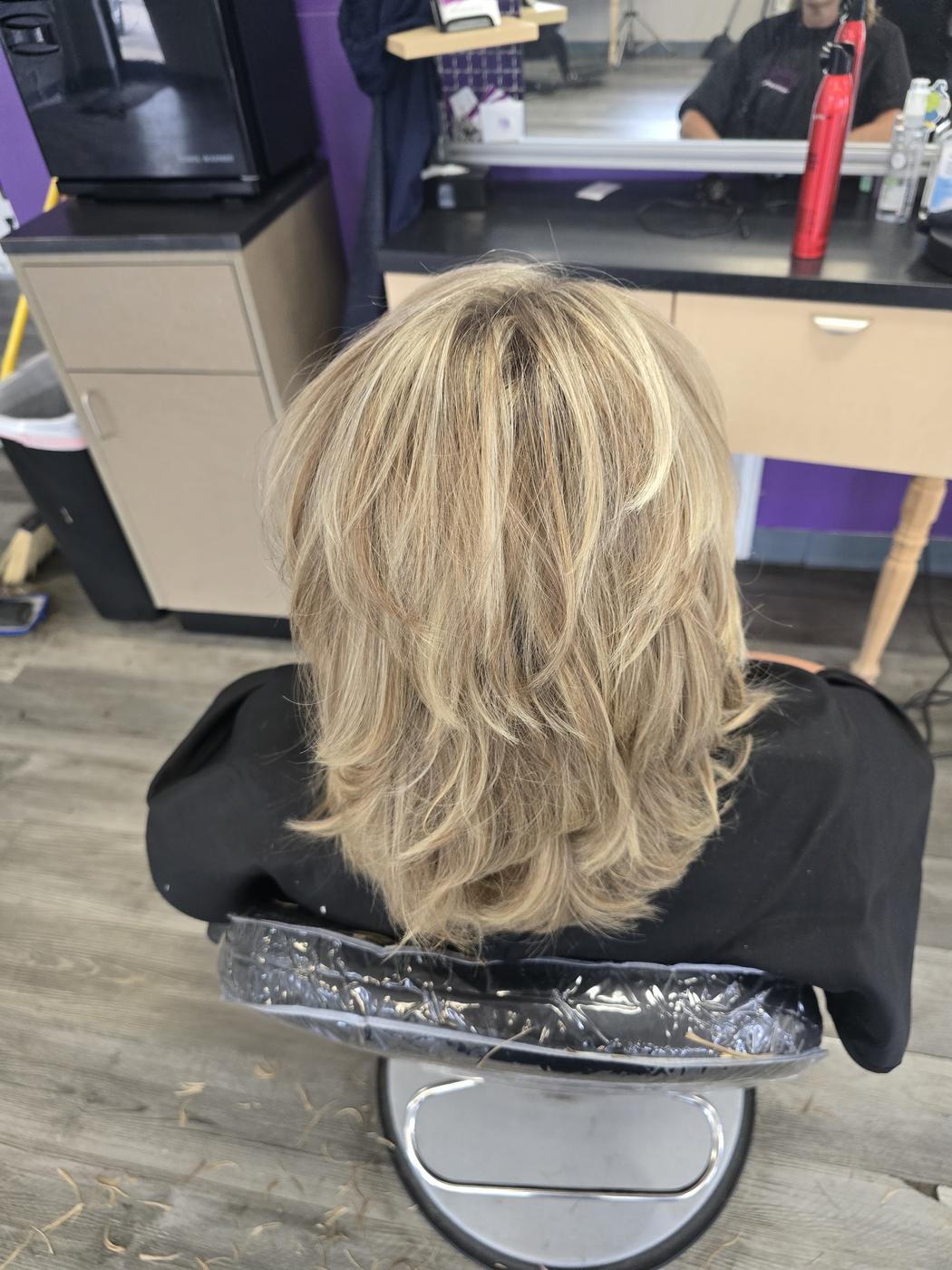 A finished layered blonde haircut inside the salon, purple accent wall behind